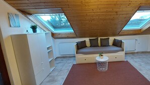 Une chambre mansardée chaleureuse, avec un plafond en pente, un lit intégré, une petite table ronde et un buffet contenant de la vaisselle.