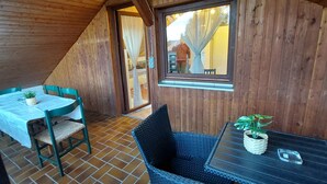 Un intérieur en bois comprenant une table à manger et des chaises, une petite table avec une plante, et une fenêtre avec des rideaux.