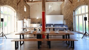 A spacious hall with wooden tables set for dining, stone walls, and large windows allowing natural light. - A resort for groups surrounded by nature (Lavoine)