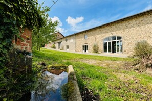 Un bâtiment en pierre avec une cour verdoyante et un petit étang.