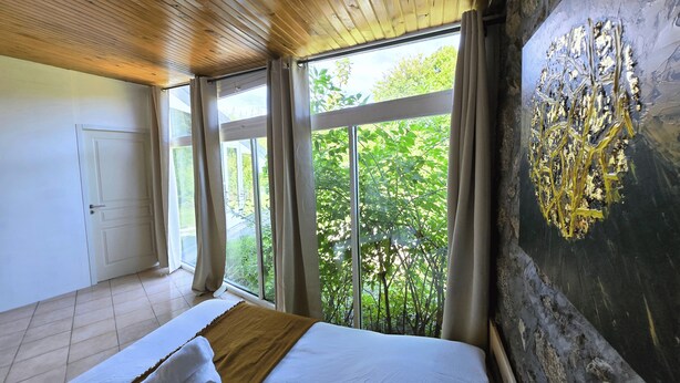 A bedroom with a large bed, a view of greenery outside, and a wooden ceiling. - A resort for groups surrounded by nature (Lavoine)