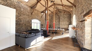 A spacious room with a stone wall, wooden beams, a sofa, a table, and a fireplace. - A resort for groups surrounded by nature (Lavoine)