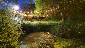 A serene outdoor setting with a small stream, surrounded by lush greenery and illuminated by string lights. - A resort for groups surrounded by nature (Lavoine)
