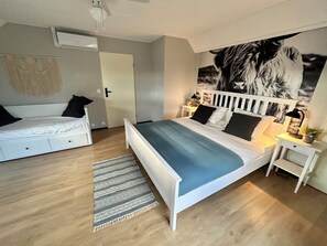 Ein Schlafzimmer mit Bett, Sofa, Nachttisch, Wand-Klimaanlage und einem gemusterten Teppich.