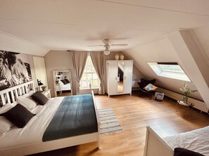 Ein Schlafzimmer mit Bett, Kleiderschrank, Schreibtisch, Stuhl, Deckenventilator und Dachfenster.