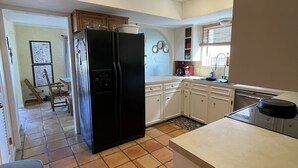 A kitchen with a black refrigerator, white cabinets, a tiled floor, and a window with blinds. - North Padre Island waterfront canal home w/private pool and dock (Corpus Christi)