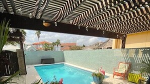 A swimming pool with a tiled deck, surrounded by potted plants and outdoor furniture. - North Padre Island waterfront canal home w/private pool and dock (Corpus Christi)