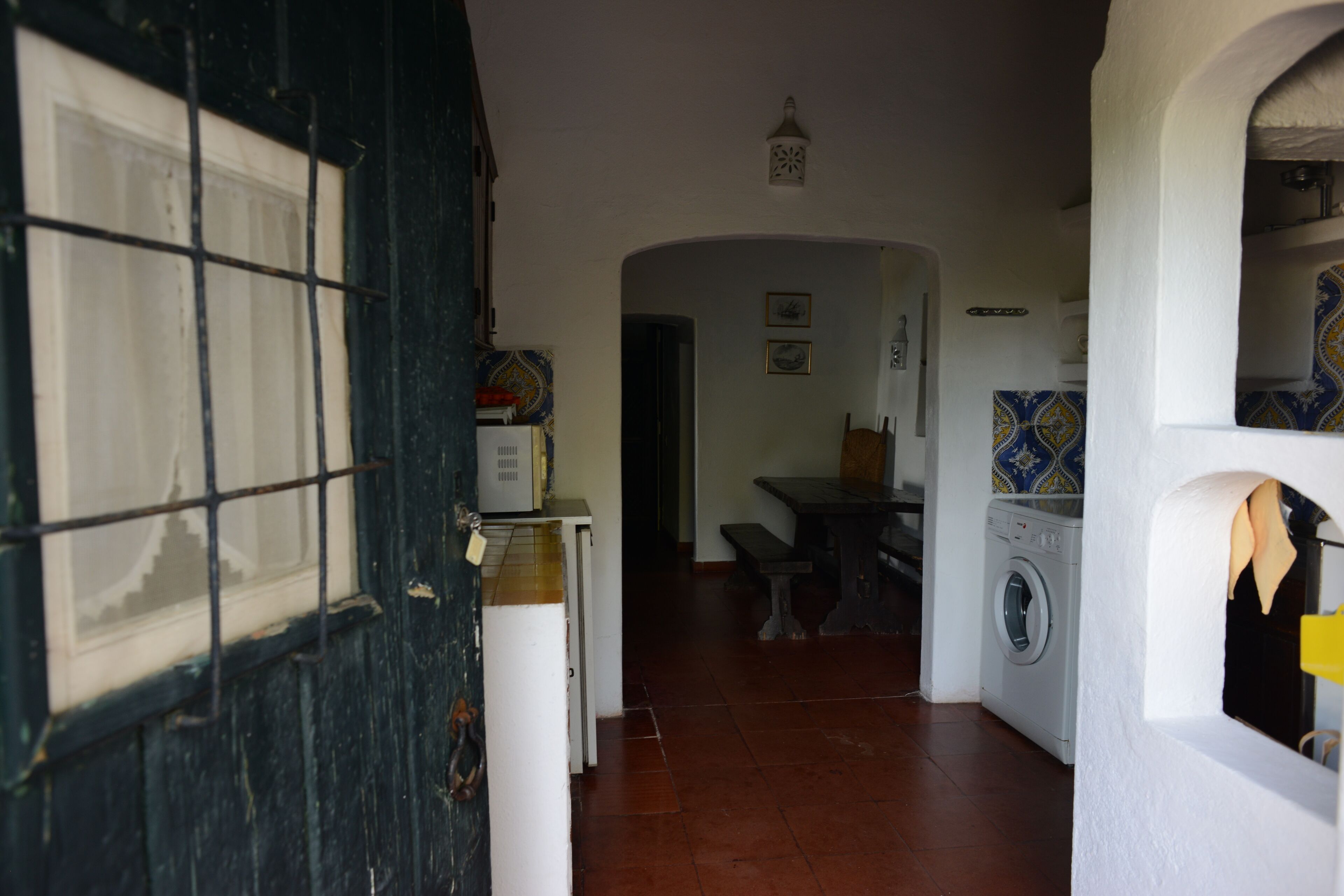 A narrow hallway with a washing machine, a tiled wall, and a door with a grid pattern.