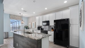 A modern kitchen with white cabinets, a black refrigerator, and a granite island. - Extrended Pool Deck/No Rear Neighbors/Windsor Hills Resort, 3 Miles to Disney®! (Kissimmee)