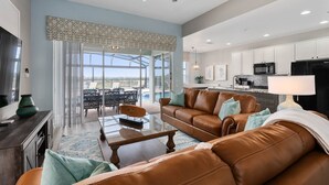 A spacious living room with a brown leather sofa, a glass coffee table, and a dining area with a glass top table and chairs. There is a kitchen area with white cabinets and a black refrigerator. - Extrended Pool Deck/No Rear Neighbors/Windsor Hills Resort, 3 Miles to Disney®! (Kissimmee)