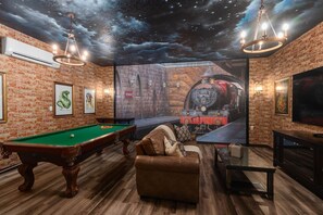A room with a pool table, a sofa, a television, and a mural of a train on the wall.