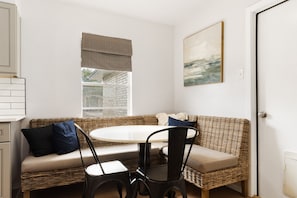 Une pièce chaleureuse avec une table ronde, un canapé en osier et une fenêtre donnant sur un bâtiment en briques.