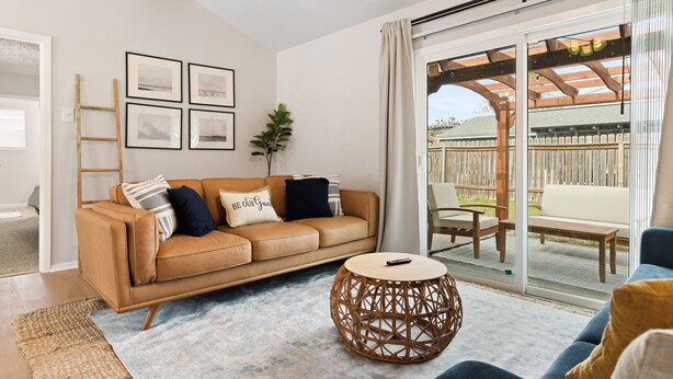 A modern living room with a leather sofa, a round wicker coffee table, and a sliding glass door leading to an outdoor patio.