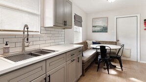 A kitchen with a sink, cabinets, and a window with blinds. There is a dining area with a table and chairs.
