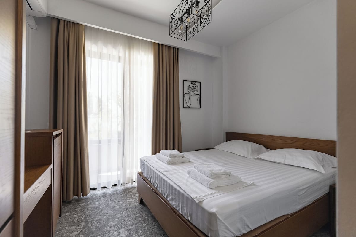 Une chambre d’hôtel avec un lit, une table de chevet en bois, un tableau accroché au mur et une fen être avec des rideaux.