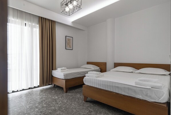 Una habitación de hotel con dos camas individuales, un ventanal con cortinas translúcidas, una obra de arte enmarcada en la pared y una lámpara moderna.