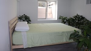 A bedroom with a bed, a window, and two potted plants. - Hamptons Apartment in Lower Part of a House (Hampton Bays)