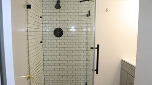 A glass-enclosed shower with white subway tiles, a handheld showerhead, and a wall-mounted faucet. - Hamptons Apartment in Lower Part of a House (Hampton Bays)