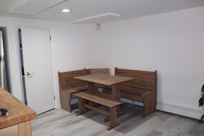 Una habitación con una mesa y banco de madera, una puerta blanca y una planta.