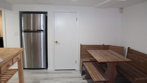 A compact kitchen with a stainless steel refrigerator, a wooden dining table with benches, and a white door. - Hamptons Apartment in Lower Part of a House (Hampton Bays)