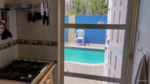 Una cocina con estufa a gas, utensilios de cocina colgantes y vistas a una piscina a través de una ventana.