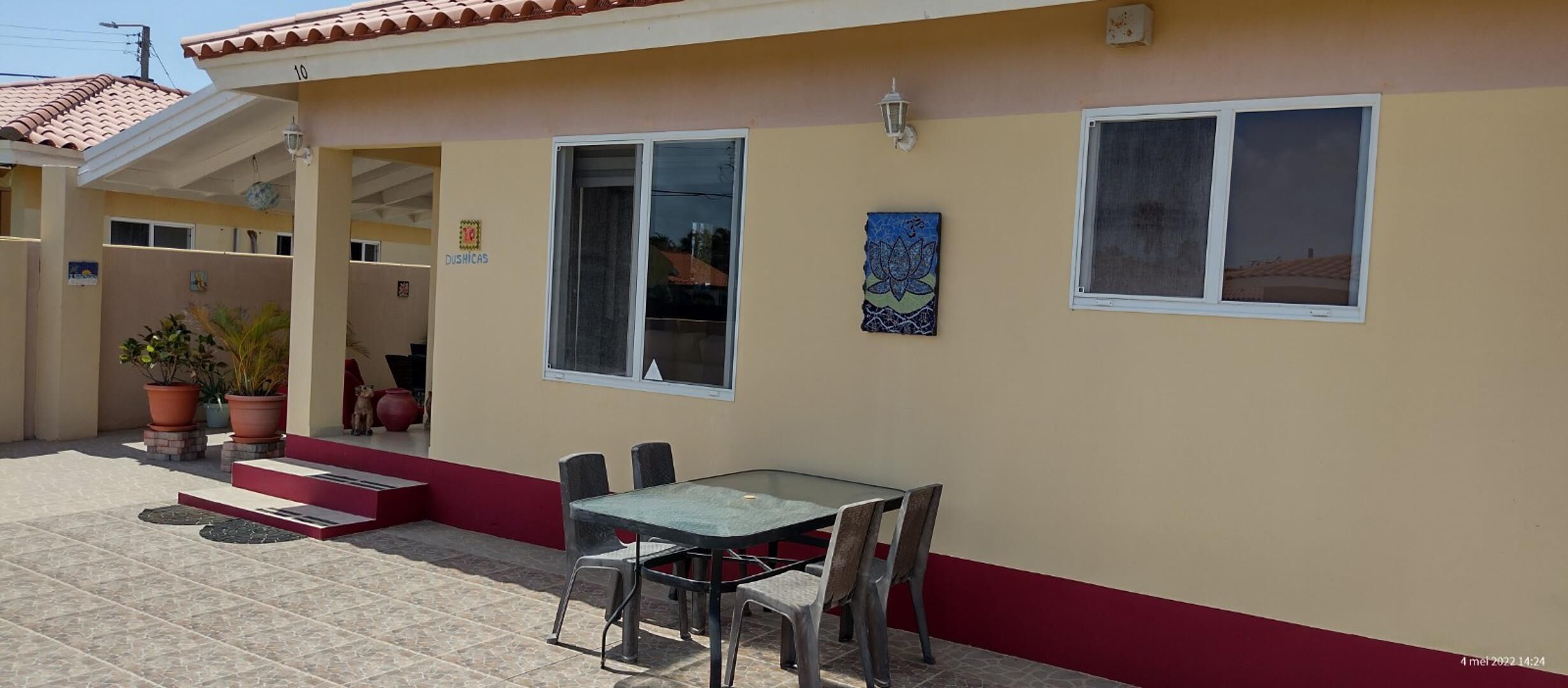 Un edificio con tejado de baldosas, una mesa de vidrio con sillas y una pared de color rojo y beige.
