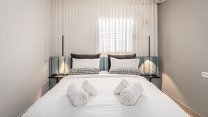 A hotel room with a large bed, two bedside tables, a nightstand, a wall-mounted air conditioner, and sheer curtains. - Superb 1Bdr w balcony (Jerusalem)