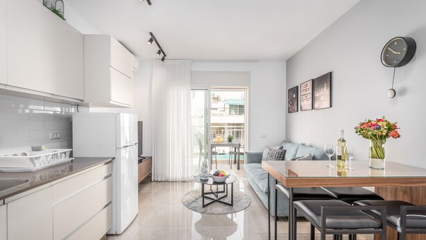 A modern kitchen with white cabinets, a refrigerator, and a dining area with a wooden table and black chairs. - Superb 1Bdr w balcony (Jerusalem)