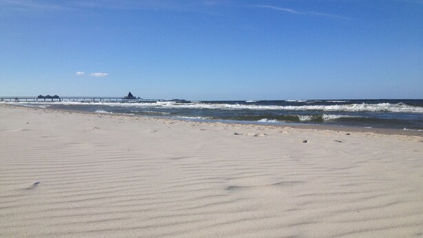 Een zandstrand met rustige golven en een pier in de verte.