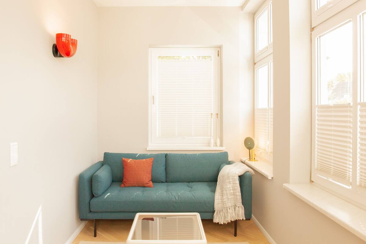 Una sala de estar con un sofá azul turquesa, un radiador blanco y una ventana con persianas.