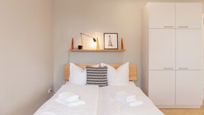 Een hotelkamer met een bed, twee kussens, een nachtkastje met een lamp, een lijst met een afbeelding en een kledingkast.