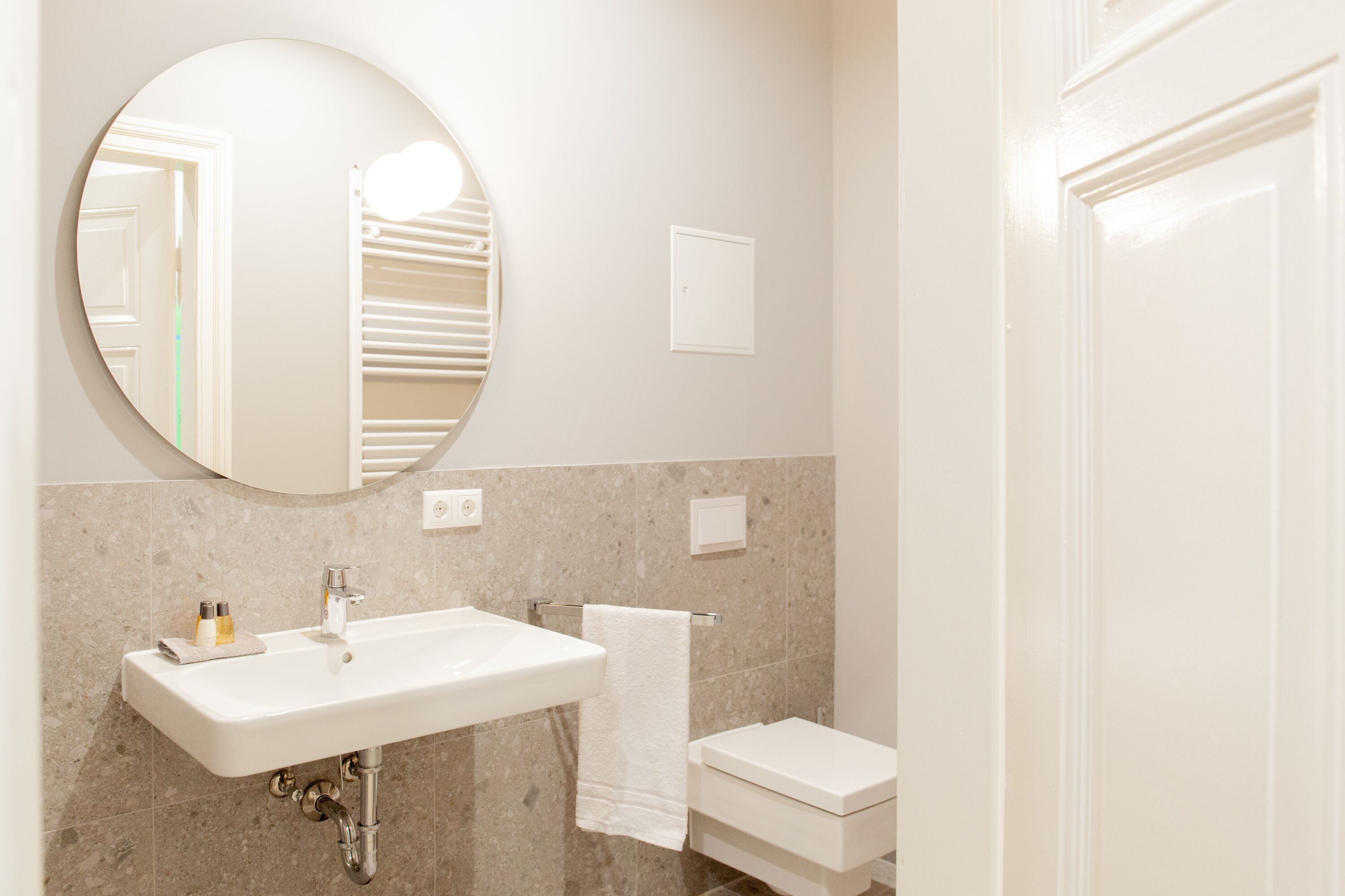 A bathroom with a round mirror, a sink, a toilet, and a towel hanging on the wall.