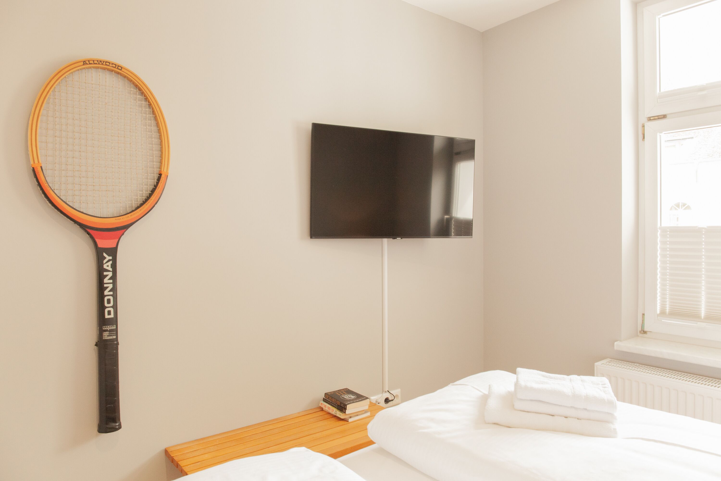 Una habitación de hotel con una cama, un televisor montado en la pared y una raqueta de tenis colgada.