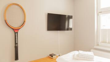 Una habitación de hotel con una cama, un televisor montado en la pared y una raqueta de tenis colgada.