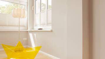 Une pièce avec une chaise jaune vif, une lampe suspendue et une fenêtre avec des stores.