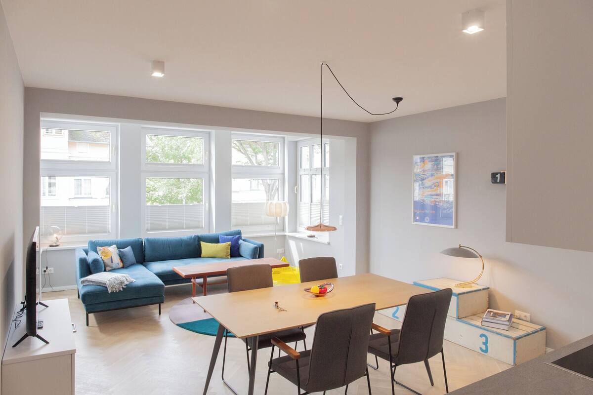 Una sala moderna con un sofá azul, una mesa de comedor de madera y un ventanal grande.