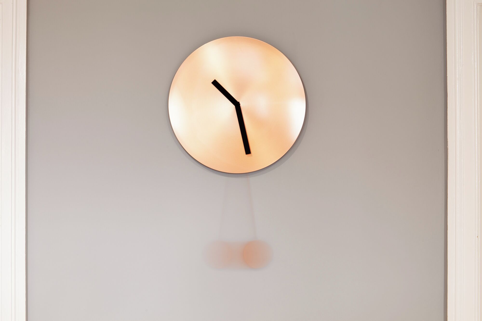 A wall-mounted round clock with a minimalist design, featuring a single black hand and no numbers.