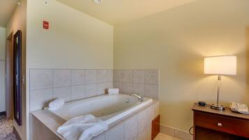 A modern bathroom with a large bathtub, a vanity with a mirror, and a bedside lamp.