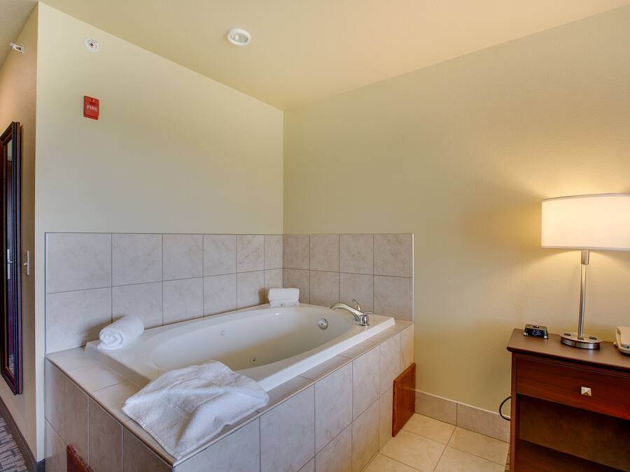 A modern bathroom with a large bathtub, a vanity with a mirror, and a bedside lamp.
