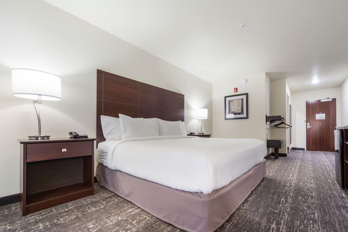 A hotel room with a large bed, bedside tables with lamps, a wardrobe, and a door leading to another room.