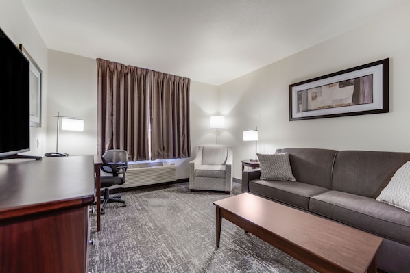 A hotel room with a desk, chair, sofa, and a large window with curtains.