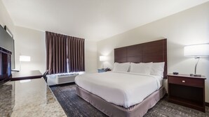 A hotel room with a large bed, a flat-screen TV, a desk with a lamp, and a window with curtains. - Cobblestone Inn & Suites-Fremont (Fremont)