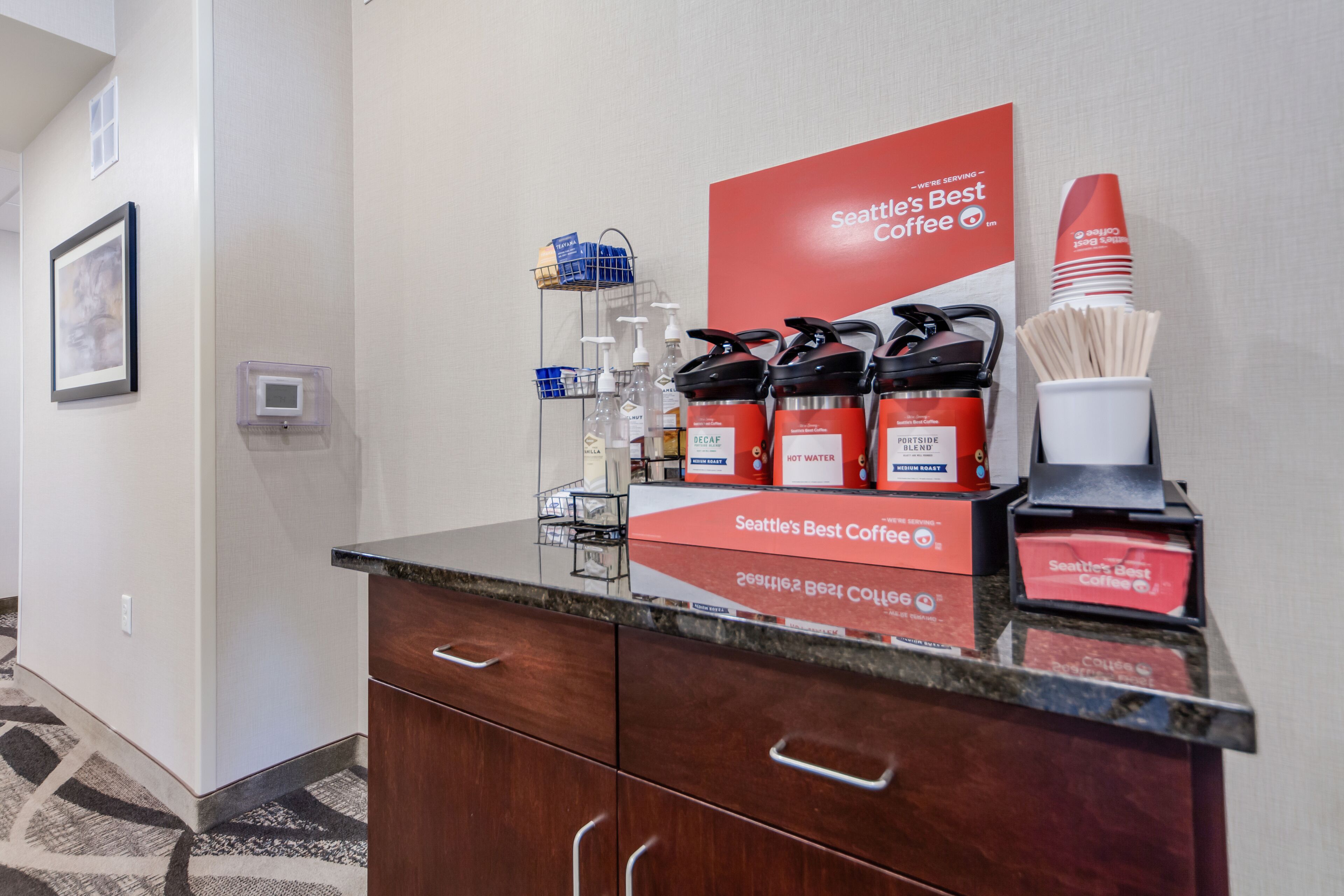 A coffee station with Seattle's Best Coffee branded dispensers, a coffee machine, and disposable cups.