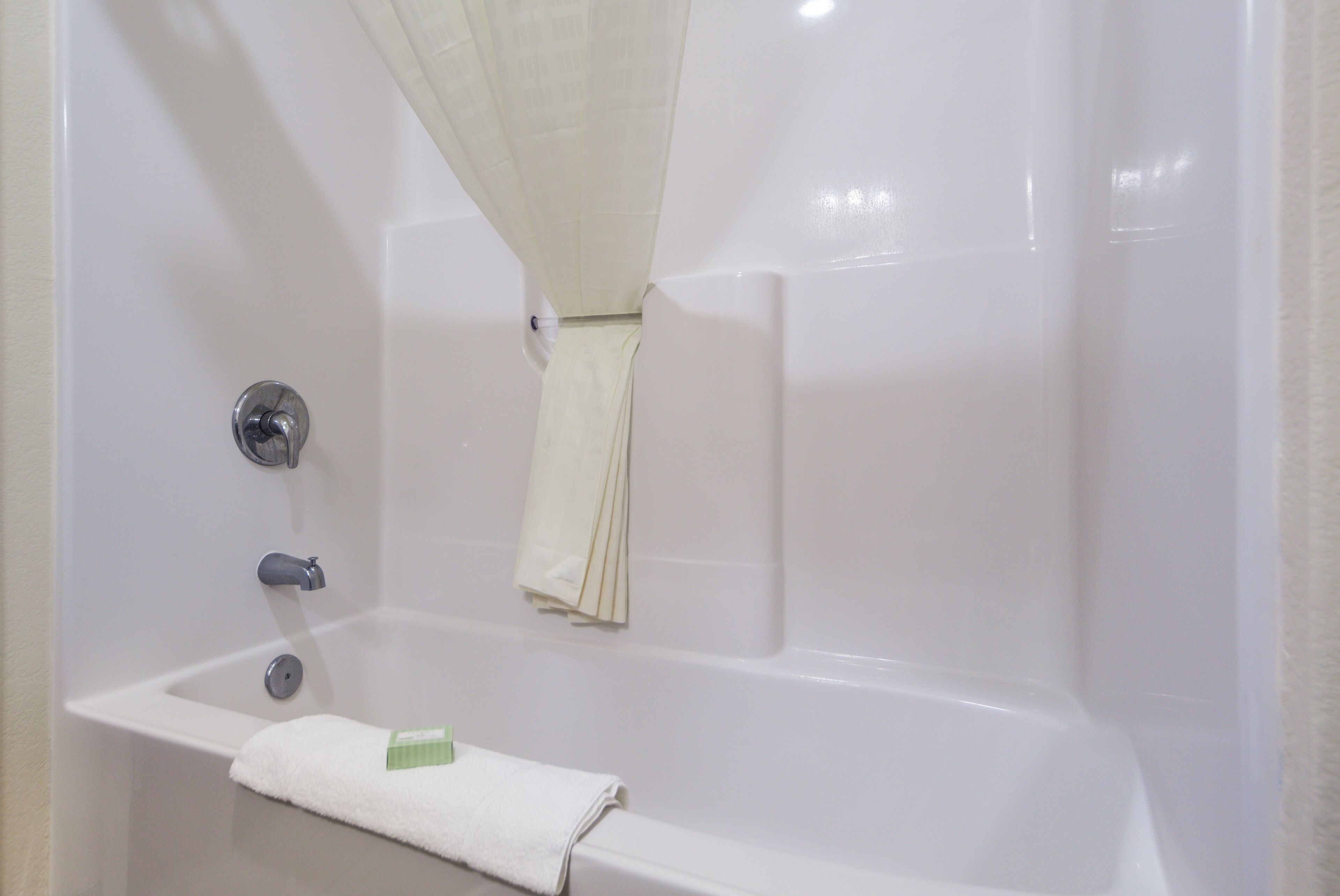 A white bathtub with a shower curtain, a towel, and a green bar of soap.