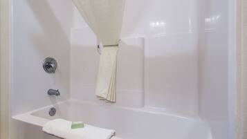 A white bathtub with a shower curtain, a towel, and a green bar of soap.