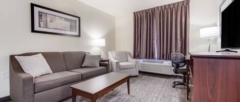 Habitación de hotel con sofá, sillón, escritorio y televisor.
