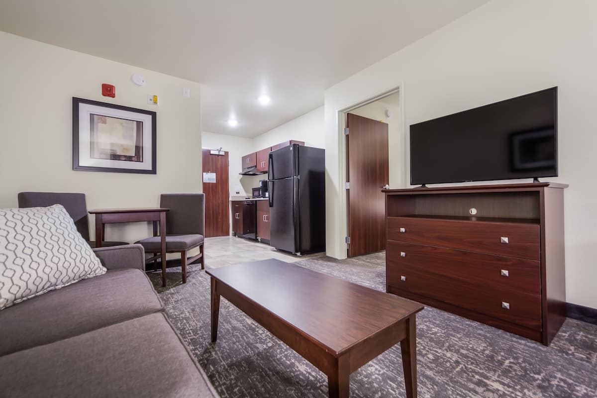 A living room with a sofa, a coffee table, a TV, and a kitchen area with cabinets and a refrigerator.
