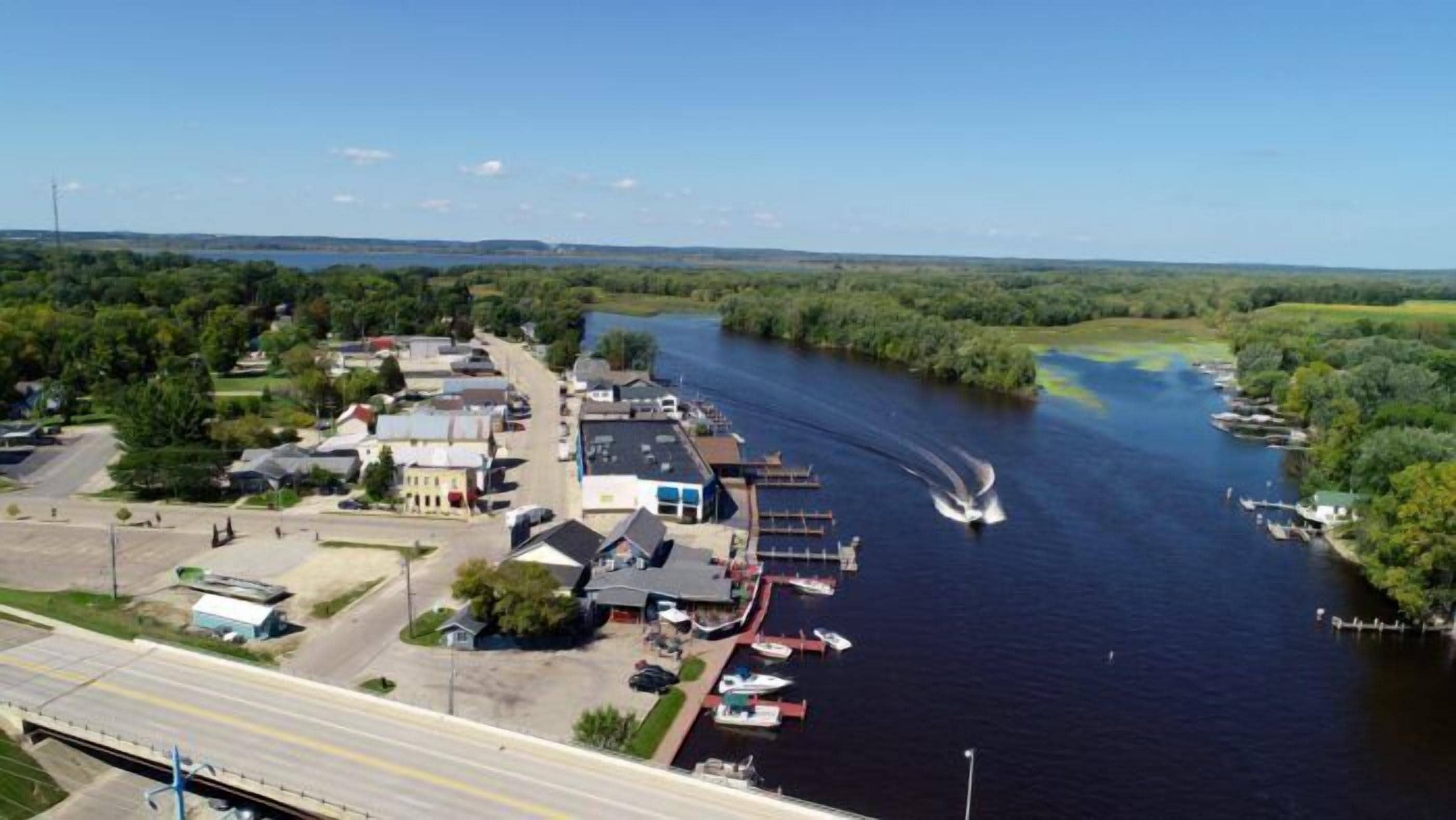 A riverside town with a dock, boats, and buildings along the water.