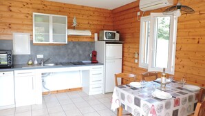 Cocina compacta con microondas, tostadora y lavabo. Hay una mesa de comedor con sillas y una ventana con persianas.