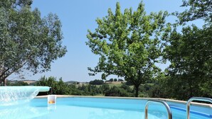 Una piscina con cubierta de madera y barandillas metálicas, rodeada de árboles y vistas a colinas ondulantes.